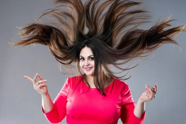 Plus-Size-Modell mit langen Haaren, die im Wind wehen, brünette, dicke Frau auf grauem Hintergrund, körperbetontes Konzept — Stockfoto