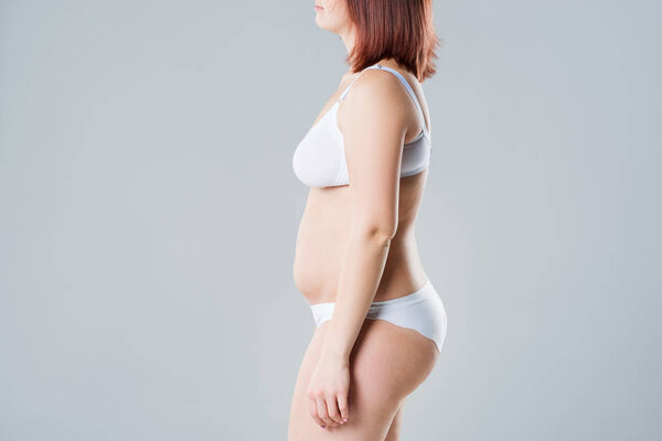 Woman with fat flabby belly, overweight female body on gray background