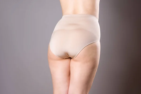 Жінка в виправних трусиках, надмірна вага жіночого тіла у формі одягу на сірому фоні — стокове фото