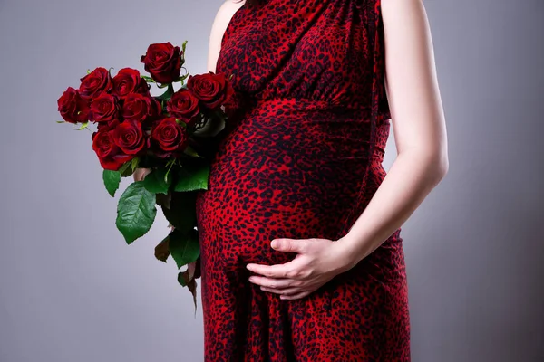 Беременная женщина с букетом красных роз на сером фоне — стоковое фото