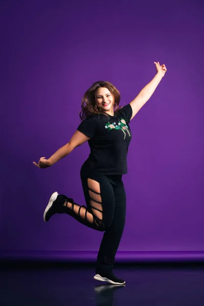 Plus size model in sportswear jumping in studio, fat woman on purple background, body positive concept