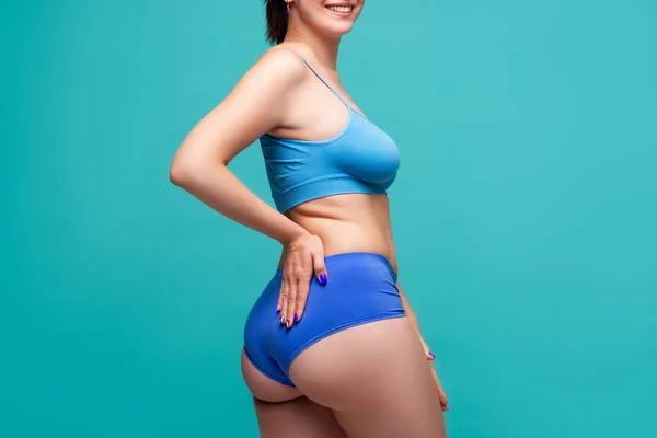 Happy beauty woman in blue underwear with big breasts and toned buttocks on turquoise background, body care concept