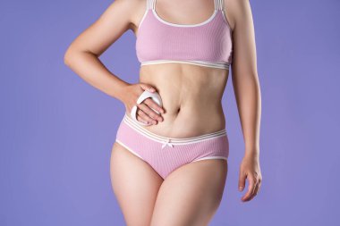 Mor arka planda masaj fırçası ile karın masajı yapan kadın, vücut bakımı konsepti