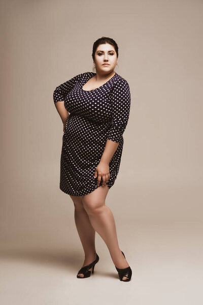 Plus size fashion model in polka dot dress, fat woman on studio background, body positive concept
