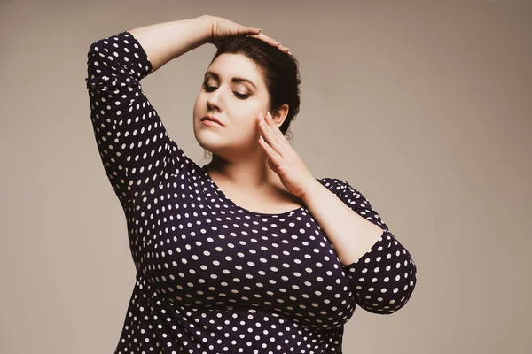 Plus size fashion model in polka dot dress, fat woman on studio background, body positive concept