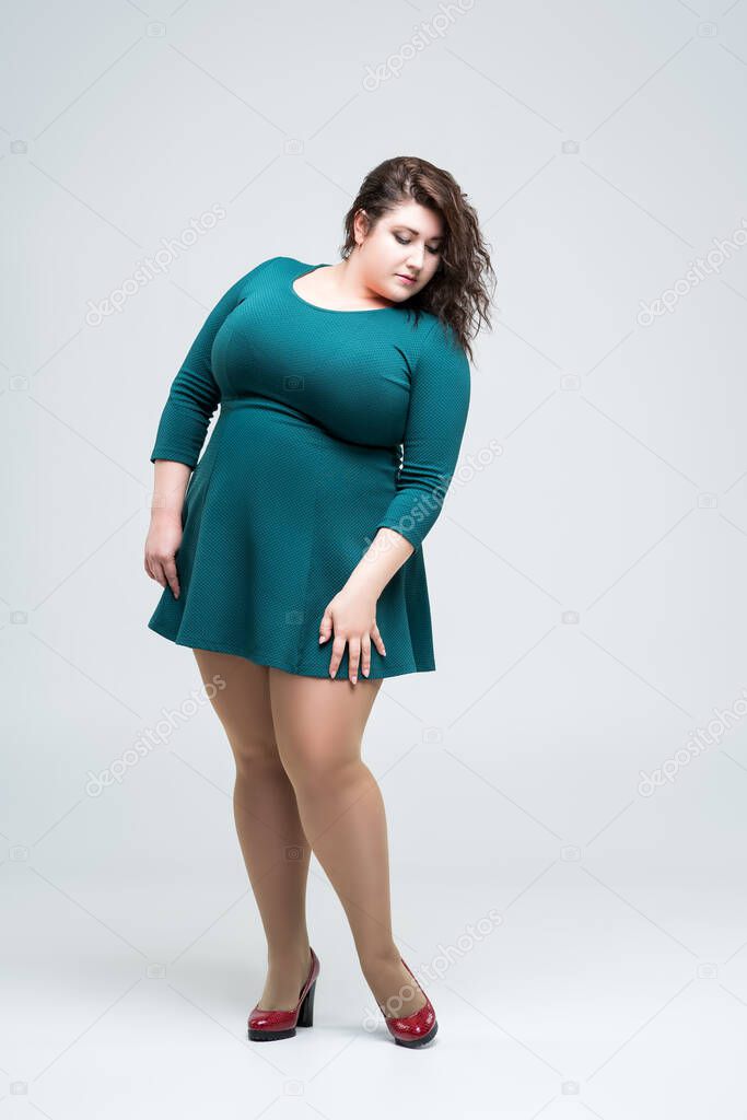 Sexy plus size fashion model in green dress, fat woman on gray background, body positive concept, full length portrait