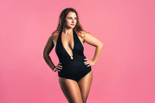 Sexy plus size fashion model in black one-piece swimsuit, fat woman in lingerie on pink background, body positive concept