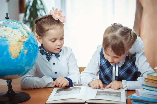 Zwei Schülerinnen sitzen an einem Schreibtisch mit einer Weltkugel Stockbild