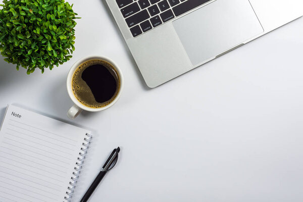 Office desk with coffee cup, blank notebook, black pen, laptop computer and plant pot, top view design