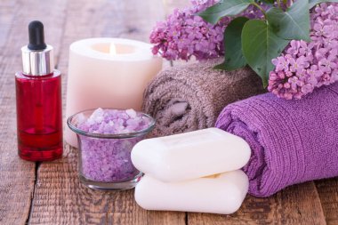 Aromatik yağ, mum, deniz tuzu, sabun, Lila çiçek ve havlu banyo yordamlar ahşap kurullarında için kase yanan kırmızı şişe. Spa ürünleri ve aksesuarları