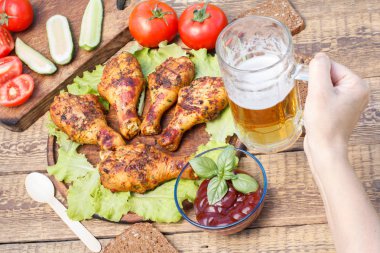Izgara tavuk budu ve marul yaprakları Ahşap Doğrama tahtası üzerinde yeşil fesleğen, cam bardak bira, taze domates ve kesilmiş salatalık tutan el ile dekore edilmiş cam kapta domates sosu