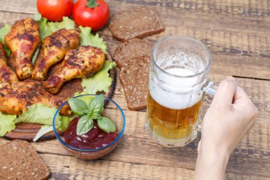 El cam kupa bira ızgara tavuk budu ve domates sosu ile dekore edilmiş Yeşil fesleğen, domates, ve arka plan üzerinde siyah ekmek ile cam kase içinde tutuyor. Kupa tarih seçici odak