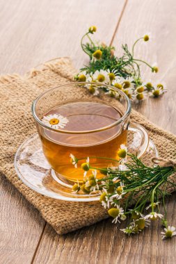 Cam bardak yeşil çay beyaz papatya çiçeği ve ahşap arka plan torba ile