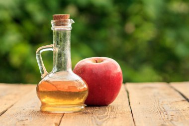 Cam şişe mantarı ve yeşil doğal arka plan bulanık ile ahşap kurullarında taze kırmızı elma ile elma sirkesi. Organik Gıda Sağlık için