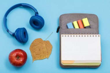 Apple, kulaklık, Kuru yaprak hissettim renkli kalemler ve mavi zemin üzerine marker ile egzersiz kitap çanta-kalem davasında açın. Üstten görünüm kopya alanı ile. Geri okul kavramı. Okul malzemeleri.
