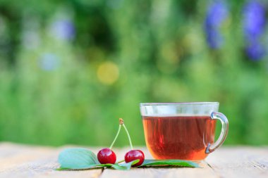 Cam bardak çay ve kırmızı olgunlaşmış kiraz meyve ile peduncles doğal arka plan bulanık eski ahşap kurullarında