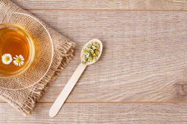 Cam fincan yeşil çay kaşığı ahşap arka plan üzerinde kuru papatya çiçeği ile. Üstten görünüm