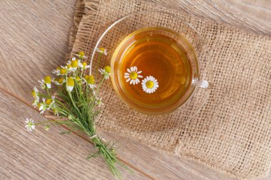 Cam bardak yeşil çay ahşap arka plan üzerinde beyaz papatya çiçeği ile. Üstten görünüm