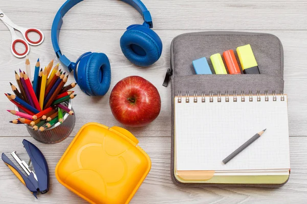 Sarı sandviç kutusu, elma, kulaklık, ileti örneği ve hissettim renk kalemler ile çanta-kalem duruma açık alıştırma kitabı ve marker gri ahşap kurullarında. Üstten görünüm. Geri okul kavramı. Okul malzemeleri.