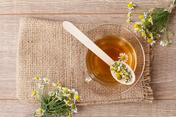 Cam bardak yeşil çay ahşap arka plan üzerinde beyaz papatya çiçeği ile. Üstten görünüm