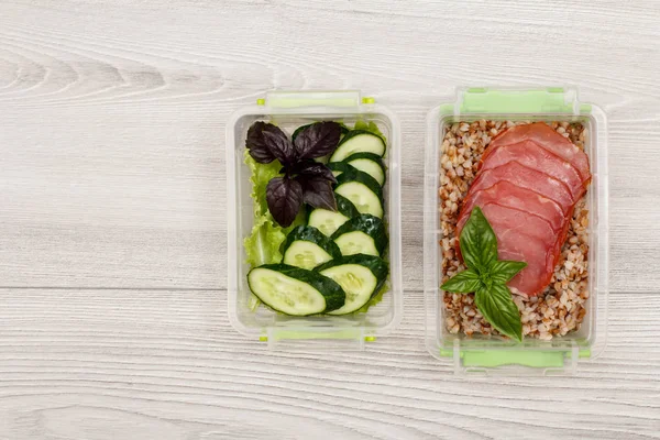 Plastik yemek kapları taze salatalık ve salata, haşlanmış Buğday lapası ve gri ahşap arka plan üzerinde et dilimleri ile hazırlayın. Kopya alanı ile üstten görünüm