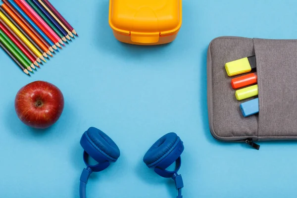 Renkli kalemler, elma, kulaklık, sandviç kutusu ve çanta-kalem case hissettim renkli kalemler ve marker üzerinde mavi arka plan ile. Üstten görünüm kopya alanı ile. Geri okul kavramı. Okul malzemeleri.