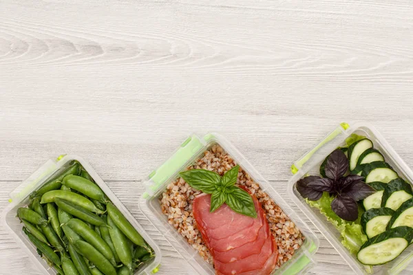 Plastik yemek kapları ile taze yeşil bezelye, haşlanmış Buğday lapası ve dilim et, salatalık ve gri arka plan üzerine salata hazırlayın. Kopya alanı ile üstten görünüm