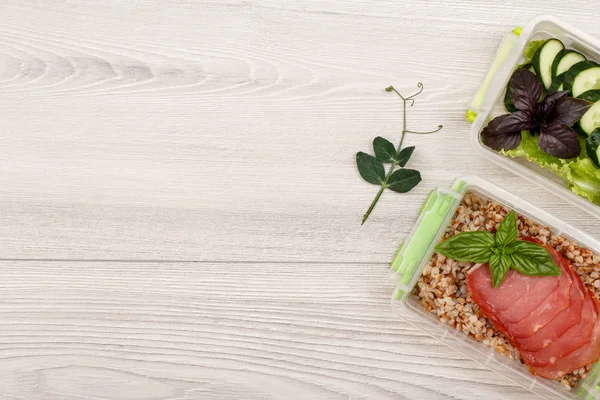 Plastik yemek kapları ile haşlanmış Buğday lapası ve dilim et, taze salatalık ve gri ahşap zemin üzerine salata hazırlayın. Kopya alanı ile üstten görünüm