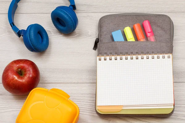 Okul malzemeleri. Sarı sandviç kutusu, elma, kulaklık, hissettim renk kalemler ile çanta-kalem duruma açık alıştırma kitabı ve marker gri ahşap kurullarında. Üstten görünüm kopya alanı ile. Geri okul kavramı