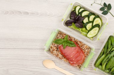 Plastik yemek kapları ile haşlanmış Buğday lapası ve et, taze salatalık ve salata, yeşil bezelye, tahta kaşık gri arka plan üzerinde dilim hazırlayın. Kopya alanı ile üstten görünüm