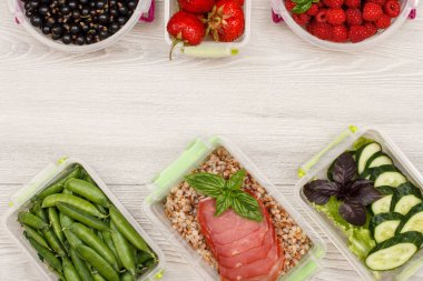 Plastik yemek hazırlık kapsayıcılar bezelye, haşlanmış Buğday lapası ve et, taze salatalık ve salata, frenk üzümü, çilek, ahududu gri arka plan üzerinde dilim ile yeşil. Üstten görünüm