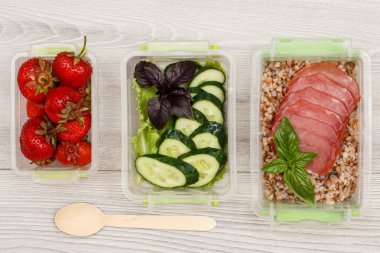 Plastik yemek kapları taze çilek, salatalık ve salata, haşlanmış Buğday lapası ve et, tahta kaşık gri ahşap zemin üzerine dilim ile hazırlayın. Üstten görünüm