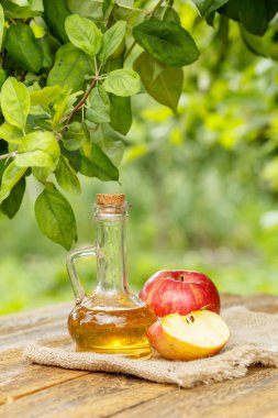 Elma sirkesi mantar ve çul üzerinde taze kırmızı elma ile cam şişe ve eski ahşap kurulları ile doğal arka plan bulanık. Organik Gıda Sağlık için