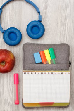 Okul malzemeleri. Açık egzersiz kitap renk ile çanta-kalem duruma kalemler ve marker, elma, kulaklık gri ahşap kurullarında hissettim. Üstten görünüm kopya alanı ile. Geri okul kavramı
