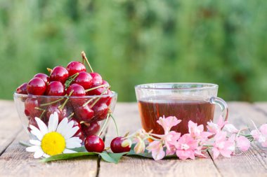Cam kase ve yeşil çay doğal arka plan bulanık ile eski ahşap kurullarında çiçekli olgun kiraz