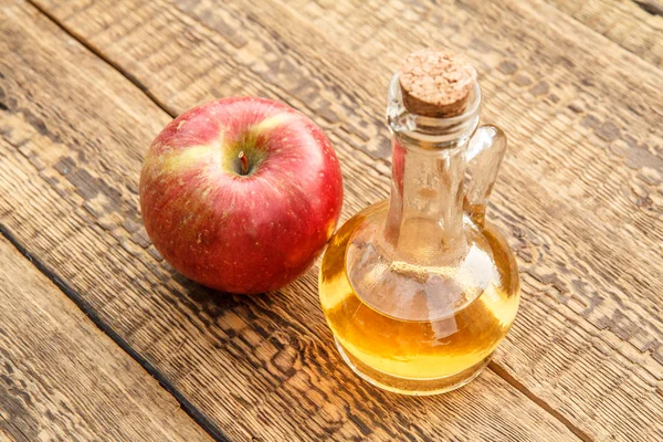 Apple vinegar in glass bottle with cork and fresh red apple on old wooden boards. Top view