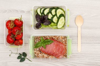 Plastik yemek kapları taze çilek, salatalık ve salata, haşlanmış Buğday lapası ve et, tahta kaşık gri ahşap zemin üzerine dilim ile hazırlayın. Kopya alanı ile üstten görünüm