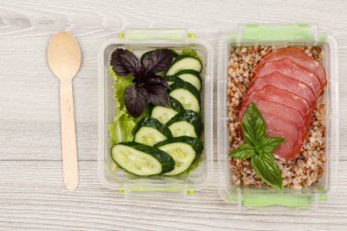 Tahta kaşık, plastik yemek kapları taze kesilmiş salatalık ve salata, haşlanmış Buğday lapası ve gri ahşap arka plan üzerinde et dilimleri ile hazırlayın. Üstten görünüm