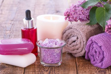 Aromatik yağ, mum, sabun, deniz tuzu, Lila çiçek ve havlu banyo yordamlar ahşap kurullarında için kase yanan kırmızı şişe. Spa ürünleri ve aksesuarları