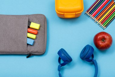 Okul malzemeleri. Çanta-kalem çalışmasıyla renk kalemler ve marker, beslenme çantası, renkli kalemler, elma ve mavi arka plan kulaklıktan hissettim. Üstten görünüm. Geri okul kavramı