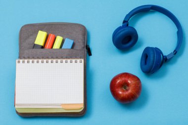 Açık egzersiz kitap renk ile çanta-kalem duruma kalemler ve marker, kulaklık ve mavi arka plan üzerinde elma hissettim. Üstten görünüm. Geri okul kavramı. Okul malzemeleri