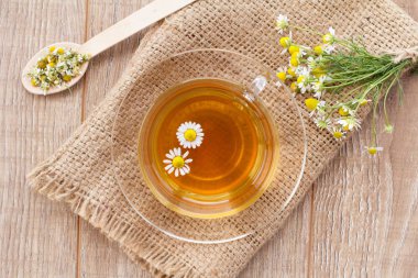 Cam bardak yeşil çay beyaz papatya çiçeği ve çanta ahşap arka plan üzerinde. Üstten görünüm