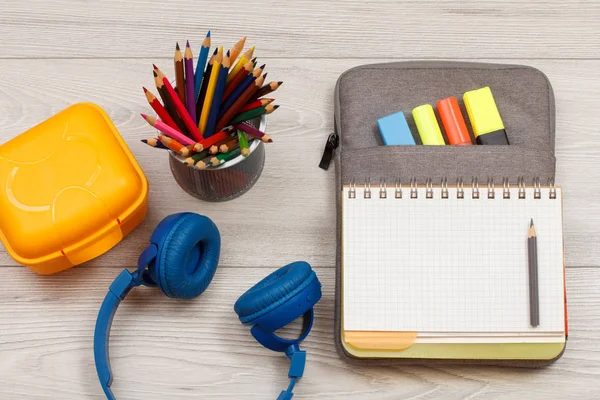 Okul malzemeleri. Kulaklıklar, sarı beslenme çantası, renkli kalemler ile kalemler için metal stand hissettim renkli kalemler ve gri ahşap kurullarında marker ile egzersiz kitap çanta-kalem dava açın. Üstten görünüm kopya alanı ile. Geri okul kavramı