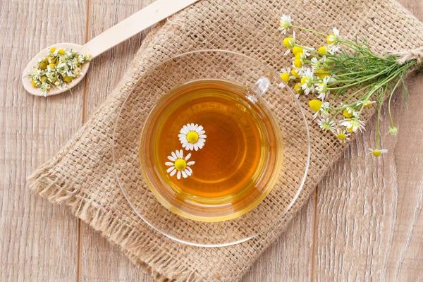 Cam bardak yeşil çay beyaz papatya çiçeği ve çanta ahşap arka plan üzerinde. Üstten görünüm