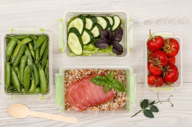 Plastik yemek kapları taze yeşil bezelye, salatalık ve salata, haşlanmış Buğday lapası ve dilim et, taze çilek ve gri arka plan üzerinde tahta kaşık ile hazırlayın. Üstten görünüm