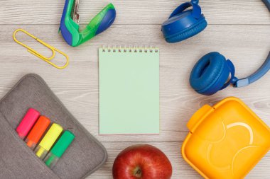 Renk modelinde çanta-kalem kalemler ve marker, elma, yeşil defter, zımba, kulaklık ve öğle yemeği kutusu gri ahşap arka plan üzerinde hissetti. Üstten görünüm kopya alanı ile. Geri okul kavramı. Okul malzemeleri.