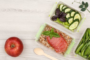 Plastik yemek kapları haşlanmış Buğday lapası ve et, salatalık ve salata, yeşil bezelye tahta kaşık ve gri arka plan üzerinde elma dilim taze çilek ile hazırlayın. Kopya alanı ile üstten görünüm