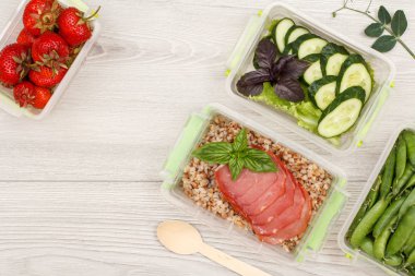 Plastik yemek kapları Buğday lapası ve dilim et, salatalık ve salata, yeşil bezelye ve gri arka plan üzerinde tahta kaşık haşlanmış taze çilek ile hazırlayın. Kopya alanı ile üstten görünüm