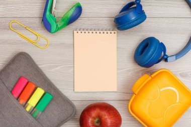 Renk modelinde çanta-kalem kalemler ve marker, elma, pembe defter, zımba, kulaklık ve öğle yemeği kutusu gri ahşap arka plan üzerinde hissetti. Üstten görünüm kopya alanı ile. Geri okul kavramı. Okul malzemeleri.