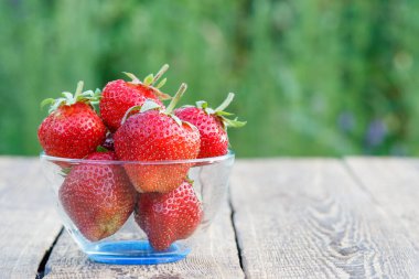 Bulanık yeşil arka plana sahip eski ahşap kurullarında cam kase kırmızı olgun çilek